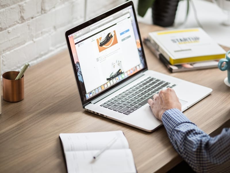 Server Speeds are Crucial to Website Development Person using a laptop on a wooden desk, with a notebook, pen, and books nearby, focused on web development. The fast servers ensure everything runs smoothly.